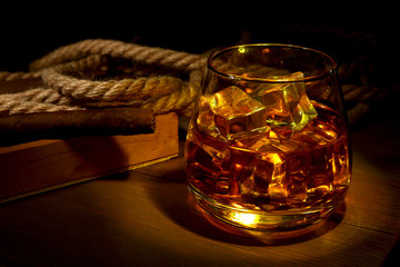 Whiskey, cognac or brandy with ice in glasses and smoking pipe on rustic wood background, copy...
