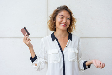 Cheerful Asian customer happy to get credit card. Beautiful young woman holding plastic card and smiling by white wall. Banking concept