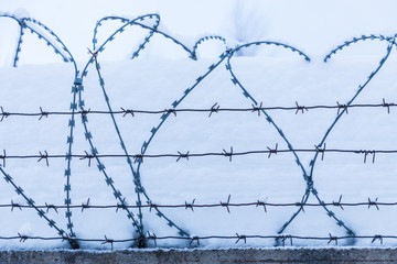 The barbed wire silhouette on the background of snow and blue sky