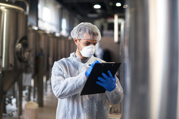 Technologist in white uniform checking quality in industrial production factory.