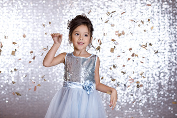 Obraz na płótnie Canvas smiling little child girl in silver dress on confetti background