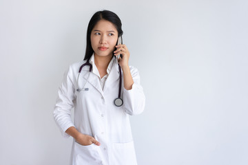 Serious female doctor talking on smartphone. Pretty young Asian woman wearing white coat and standing. Communication in medicine concept. Isolated front view on white background.