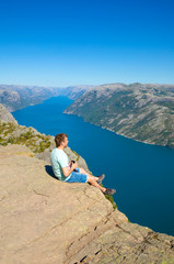 Naklejka premium Hiker standing on Preikestolen and looking on the fjerd, Preikestolen - famous cliff at the Norwegian mountains