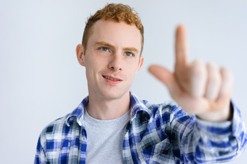 Smiling young guy touching invisible wall. Handsome business man standing and pointing at something. Promotion concept. Isolated front view on white background.