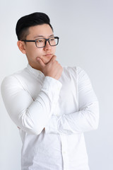 Thoughtful Asian man touching chin and looking away. Young guy standing and posing. Contemplation concept. Isolated view on white background.