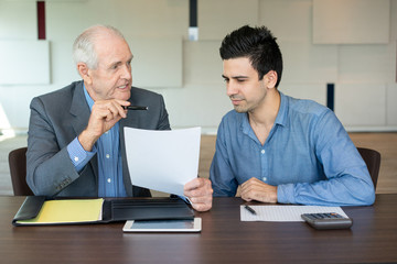 Business partners discussing contract. Serious senior entrepreneur explaining work to his young coworker. Business meeting concept