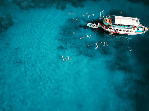 Aerial shot of beautiful blue lagoon at hot summer day with sailing boat. Top view of people swimming around the boat.