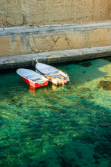 Two small fishing boats moored at the quay of the small port of Porto Miggiano. The port carved into the rock. A limpid, clear turquoise sea. Santa Cesarea Terme, Puglia, Salento, Italy.