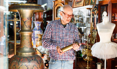Portrait of mature man choosing vintage goods at antiques shop - obrazy, fototapety, plakaty