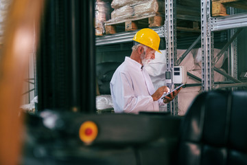 Senior worker in work wear using tablet and checking temperature in warehouse.