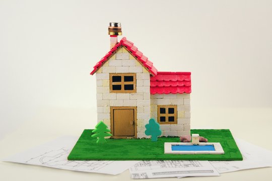 Model of a family house has coins on the chimney and stands on building plans.Model family house with swimming pool and garden. The concept of financially demanding housing.