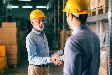 Two businessmen shaking hands for successful business while standing in warehouse.