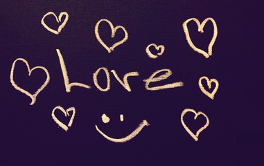 The inscription love on the board of purple hue, next to the inscription drawn heart. The inscription on the board is made of white chalk.