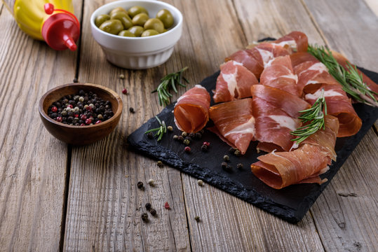 Sliced ham with olives on wooden background.