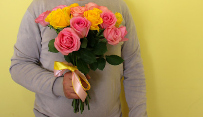 a man with pink and yellow roses in the hands on yellow background. valentine day love beautiful. Copyspace for text.
