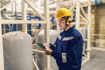 Young Caucasian man in protective suit using tablet while standing in heating plant.
