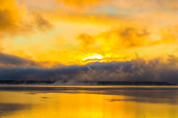 Sunrise on the lake, reflection of sun in water, with fog and clouds on summer morning