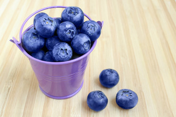 Fresh ripe blueberries in a small bucket on a wooden table with copy space for your text