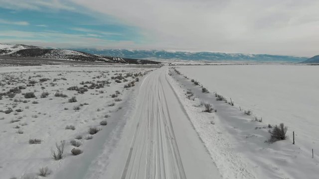 Aerial-Pull back and descending over snowy road heading toward distant mountain valley