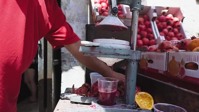 Pomegranate seller pressing the fruits. Pomegranate juice prepared on old metal juice press squeeze machine, close-up.