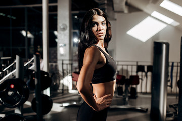 Fototapeta na wymiar Slim dark-haired girl dressed in black sport clothes is doing warm up in the gym