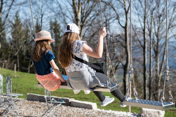 Two gorgeous blonde girls swinging on a swing on a sunny summer day