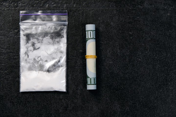 Rolled hundred dollars banknote and plastic packet of cocaine on black background, copyspace