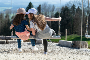 Two gorgeous blonde girls swinging on a swing on a sunny summer day