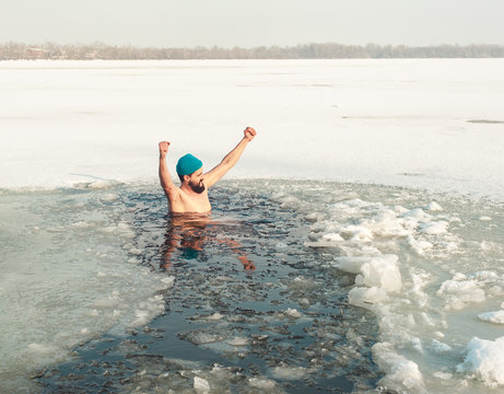 bearded man in hat in ice hole swimming