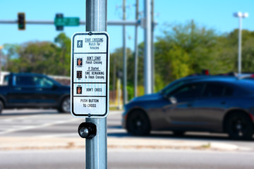 Traffic intersection pedestrian crosswalk crossing sign with signal descriptions above the request button with cars and lights in the background. - 244392836