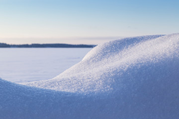 Close-up of fresh shiny snow on a snowdrift on a sunny day in the winter. Blurred frozen and snowy lake in the background.