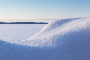 Close-up of fresh shiny snow on a snowdrift on a sunny day in the winter. Blurred frozen and snowy lake in the background.