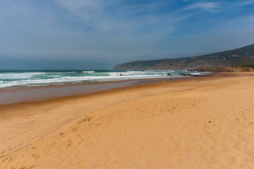 Fototapeta na wymiar Vast golden sand beach on the Portuguese coast under a moody sky. Guincho Beach landscape in Cascais, Portugal a popular destination for surfers.