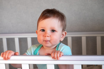 Cute baby standing in a white wooden bed. Little girl learning to stand in her crib.