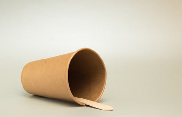 empty paper cup for coffee lies on its side on a dark background, next to it is a wooden coffee spoon