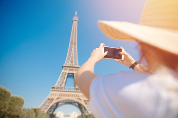 Young student girl with backpack makes photograph of Eiffel Tower in summer. Concept of learning at university exchange