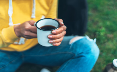 Closeup girl holding in hands cup of hot tea on green grass in outdoors nature park, beautiful woman hipster enjoy drinking cup of coffee, lifestyle relax recreation meditation concept