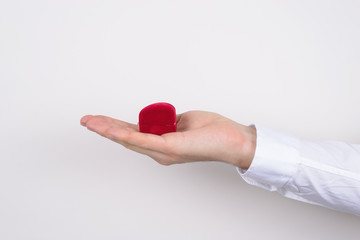 Side profile closeup cropped photo of hand holding open unpacked unwrap red heart shaped small little box with ring inside isolated grey background