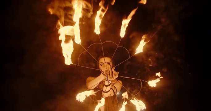 Cool female fire show stuntsman performing, swinging her burning fans, standing in circle of burning bowls- slow motion 4k