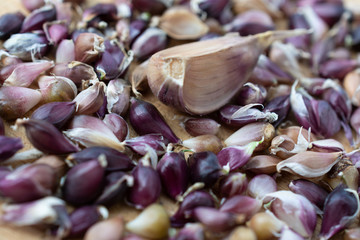 A large number of garlic seeds are on a wooden board against a clove of garlic.