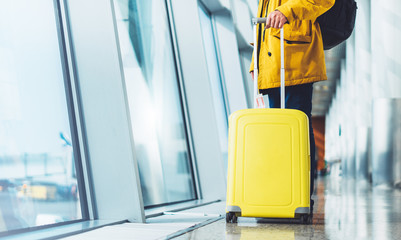 traveler tourist with yellow suitcase backpack at airport on background large window blue sky, waiting in departure lounge area, hall of ​airport terminal, vacation trip concept, empty space mockup