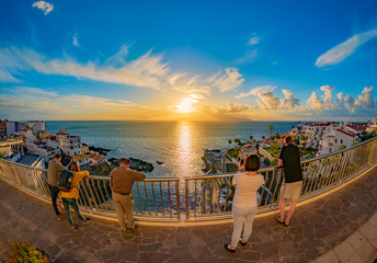 Group of people watching amazing sunset reflected in Atlantic ocean over the coast of Puerto de Santiago in Tenerife island, Spain