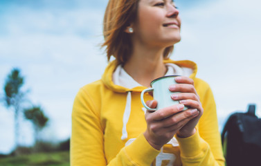 Happy smile girl holding in hands cup of hot tea on green grass in outdoors nature park, beautiful woman hipster enjoy drinking cup of coffee, lifestyle relax recreation meditation concept