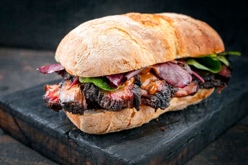 Traditional barbecue pulled pork piece of Bosten butt as sandwich with lettuce as closeup on a black board