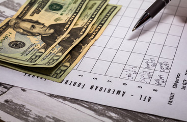 Football office pool grid for sports betting concept with money and a pen, partially completed boxes