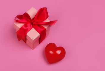 Gift or present box with red bow ribbon and glitter heart on living coral background for Valentines day