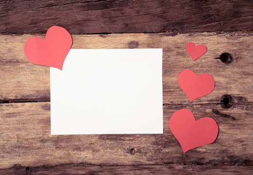 Conceptual Valentines image of white paper note with space for text and red hearts on wood table