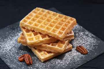 sweet tasty Belgian waffles close-up, sprinkled with powdered sugar, pecans,