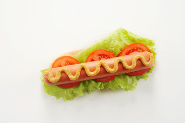 Hotdog on a white background. The top half of the bun is missing. Hotdog stuffing consists of sausage, lettuce, tomato slices, mustard and ketchup. Close-up. Macro shooting.