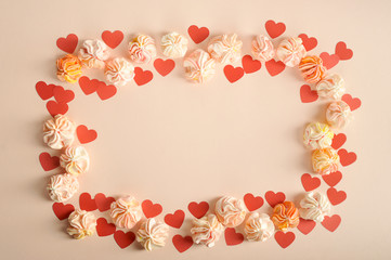 Arrangement for Valentine's Day of pink meringues and red paper hearts. Objects frame. Free space to place text. Pink background. Close-up.
